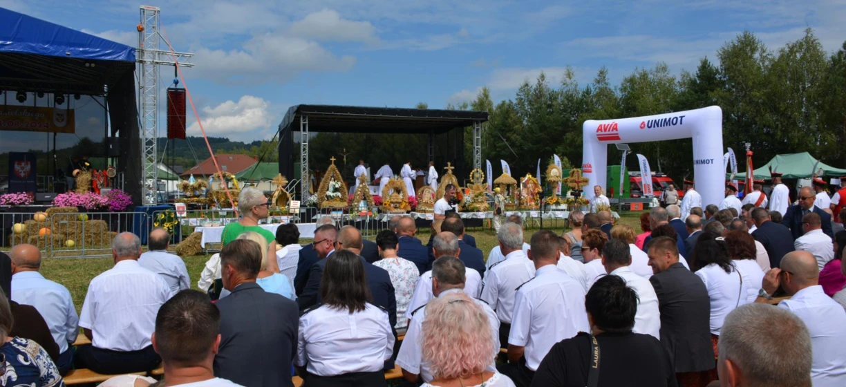 Wydarzenie publiczne z tłumem zgromadzonym przy scenie na wydarzenie społecznościowe z prelegentami i sponsorami. Polski tekst obejmuje datę "8.08.2024", "Laura B" oraz różne nazwy firm.