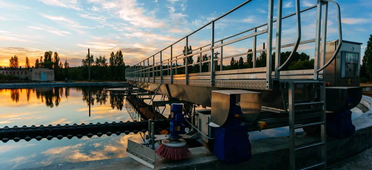 Spokojny wieczór na nabrzeżu zbiornika wodnego, gdzie promienie słońca odbijają się od wody, a poręcz prowadzi drogę. Zachód słońca rozświetla wodę i ogrodzenie ciepłym blaskiem.